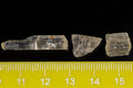 Three natural yellow scapolite crystals in daylight beside a millimetre ruler for scale